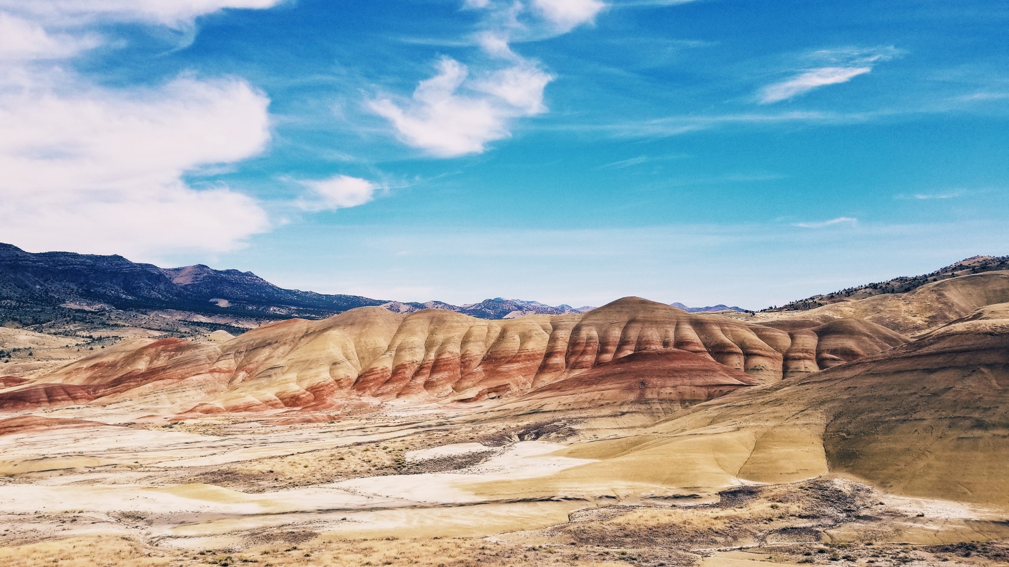 Low hills striped in red, pink and grey in the Painted Desert, Arizona, under a bright blue sky.