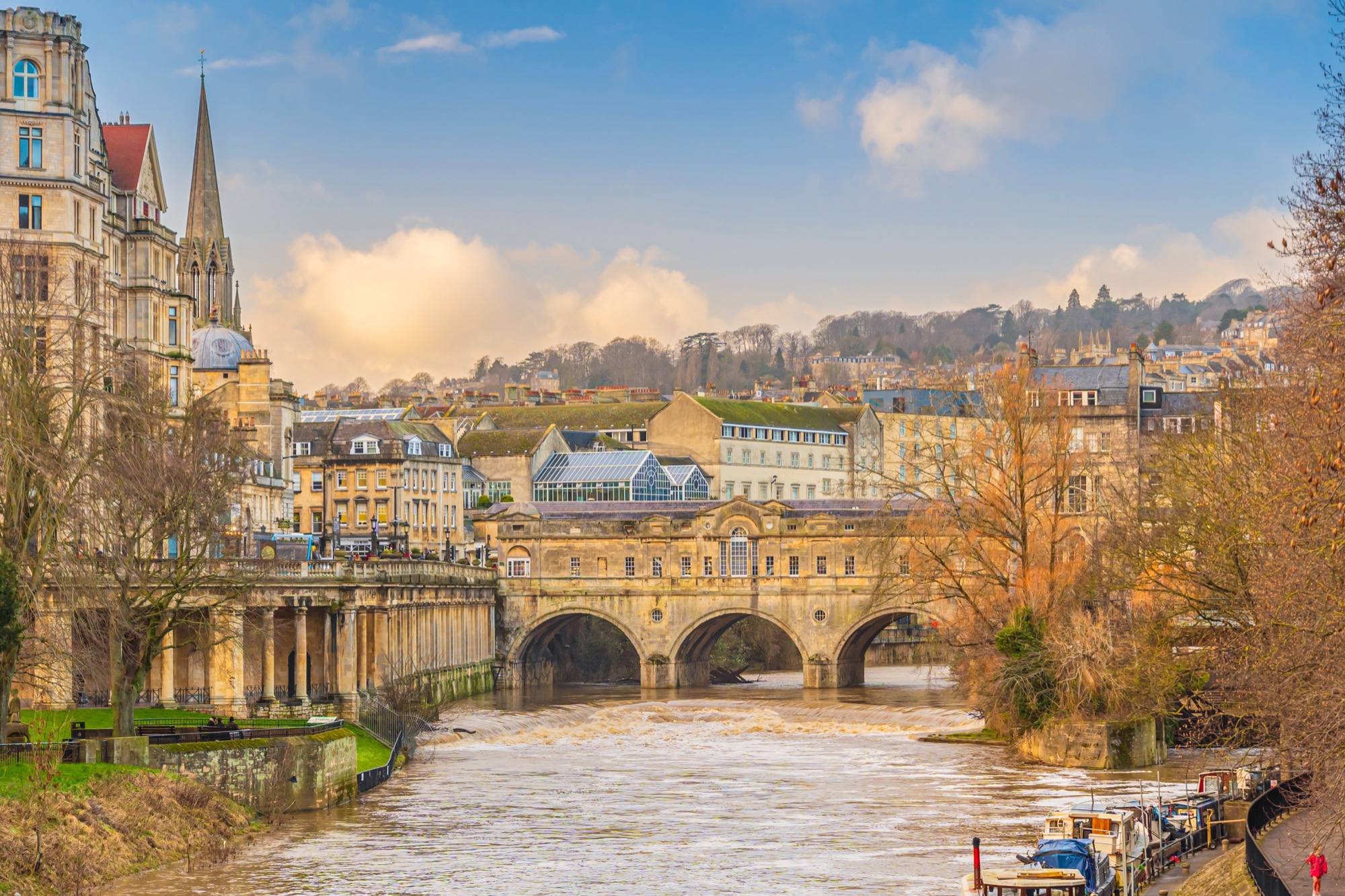 Pulteney Bridge with shops built across it, spanning the River Avon above a curved weir, with Bath's stone buildings behind.