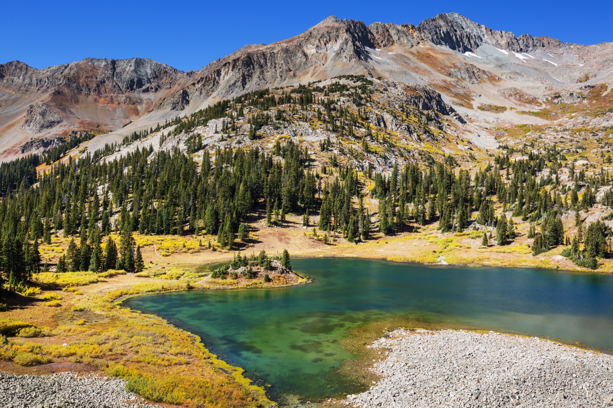 A still mountain lake below rocky peaks with patches of snow, in Colorado.