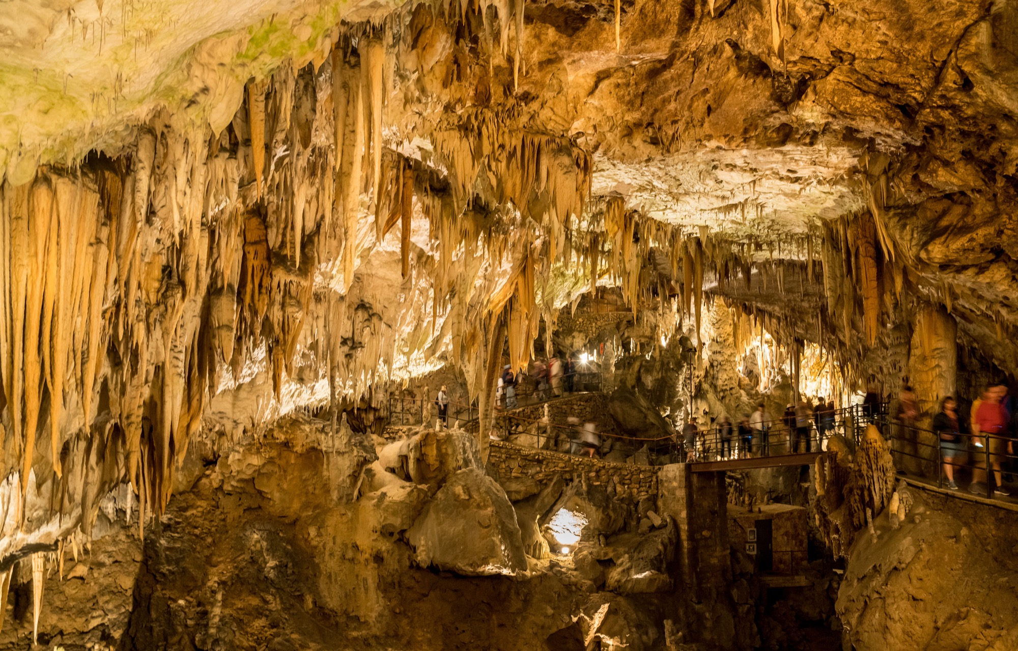 Stalactites hanging from the roof and stalagmites rising from the floor of a limestone cave, lit from below.