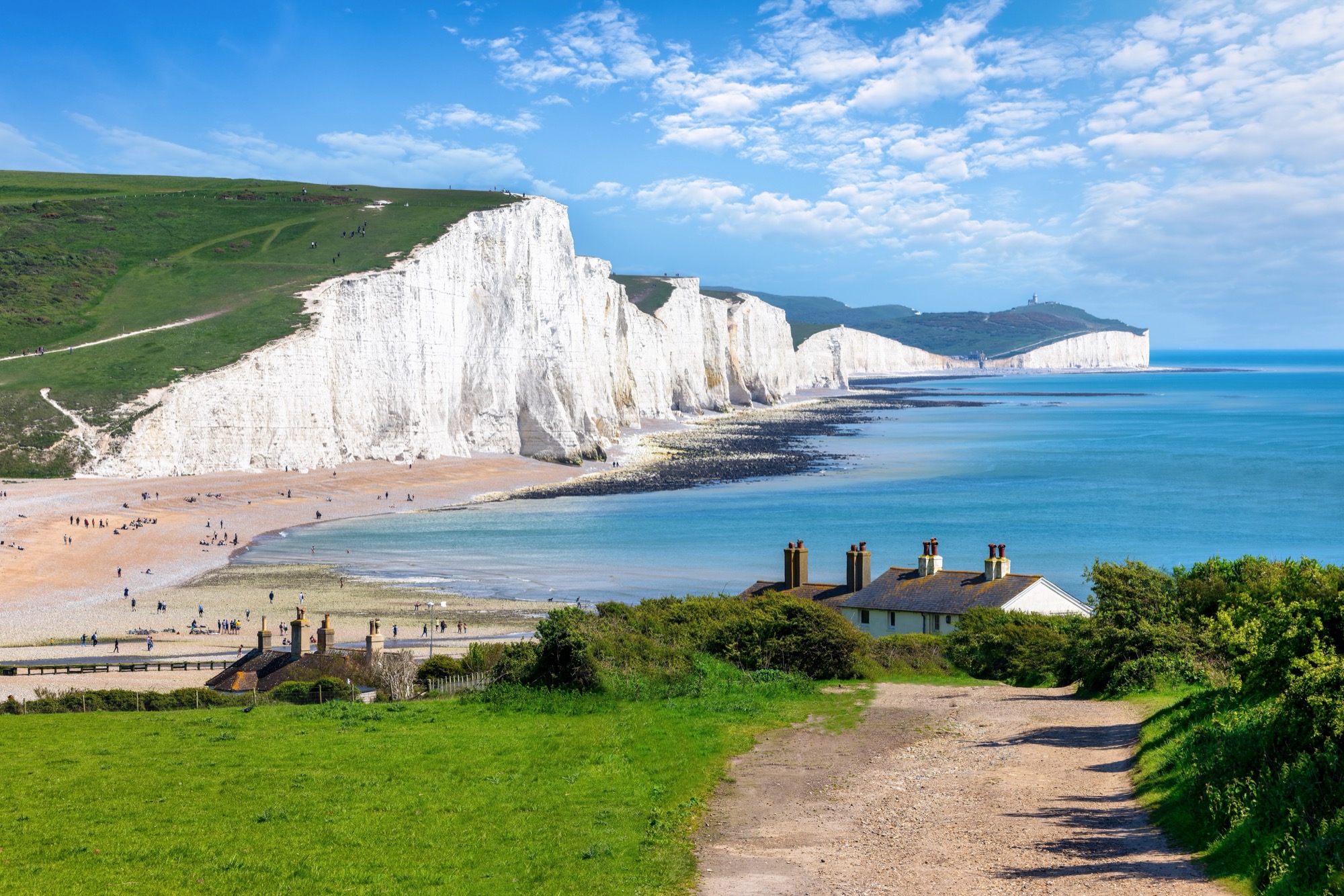 White chalk cliffs along the Sussex coast seen from Seaford Head, with coastguard cottages and a pebble beach in front.