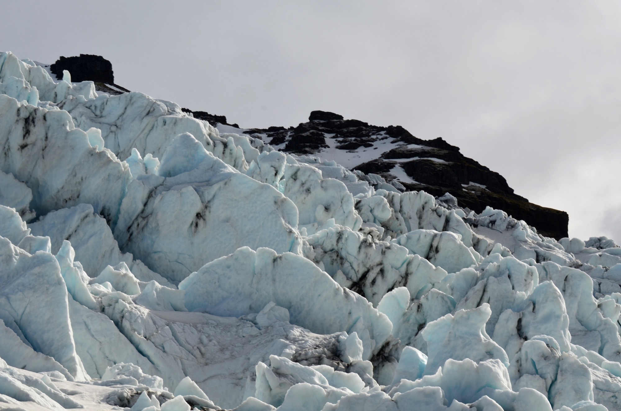 A glacier flowing between mountains, its surface cracked into ridges.