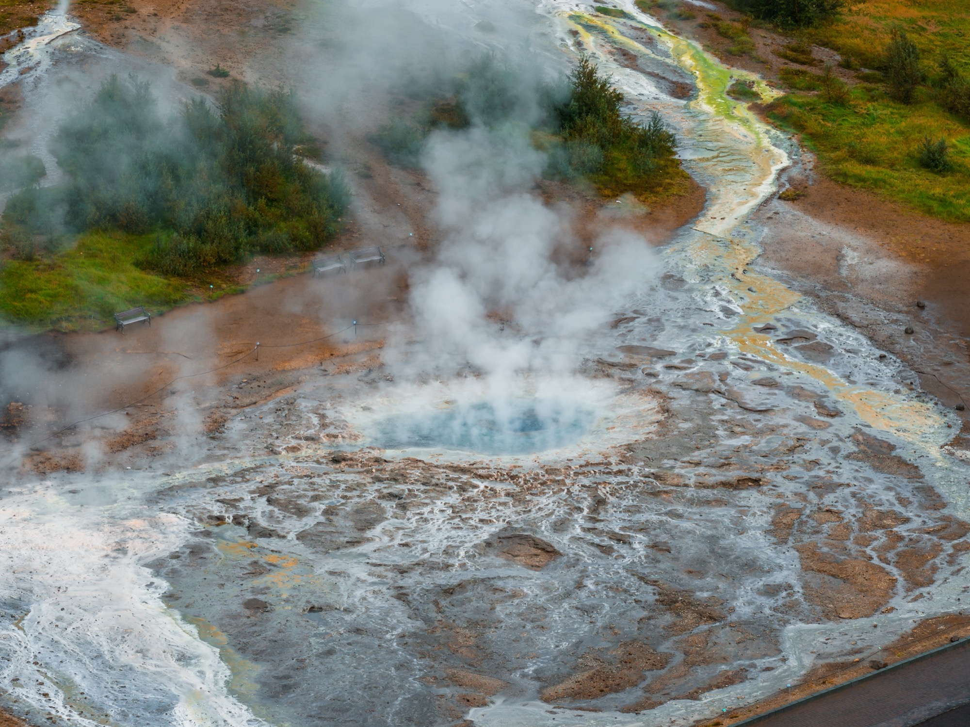 Steam rising from a geothermal hot spring pool in an open landscape.