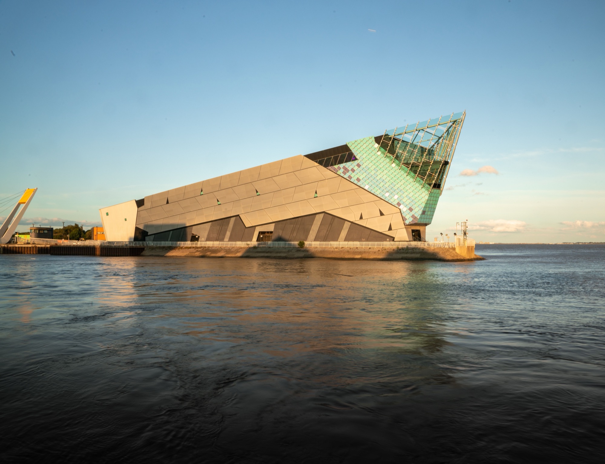 The angular glass-and-steel building of The Deep aquarium in Hull, at the edge of calm water in evening light.