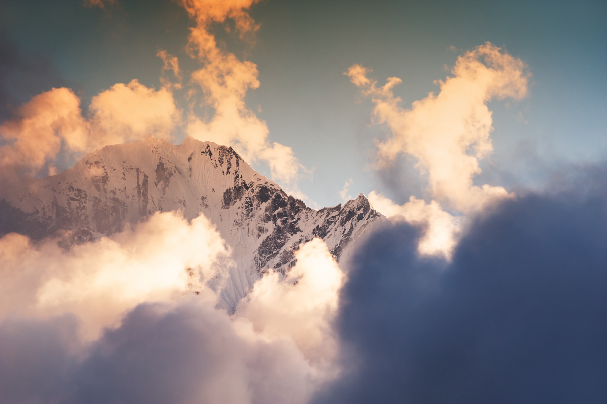 Snow-covered Himalayan peaks with clouds, lit by a low sun.