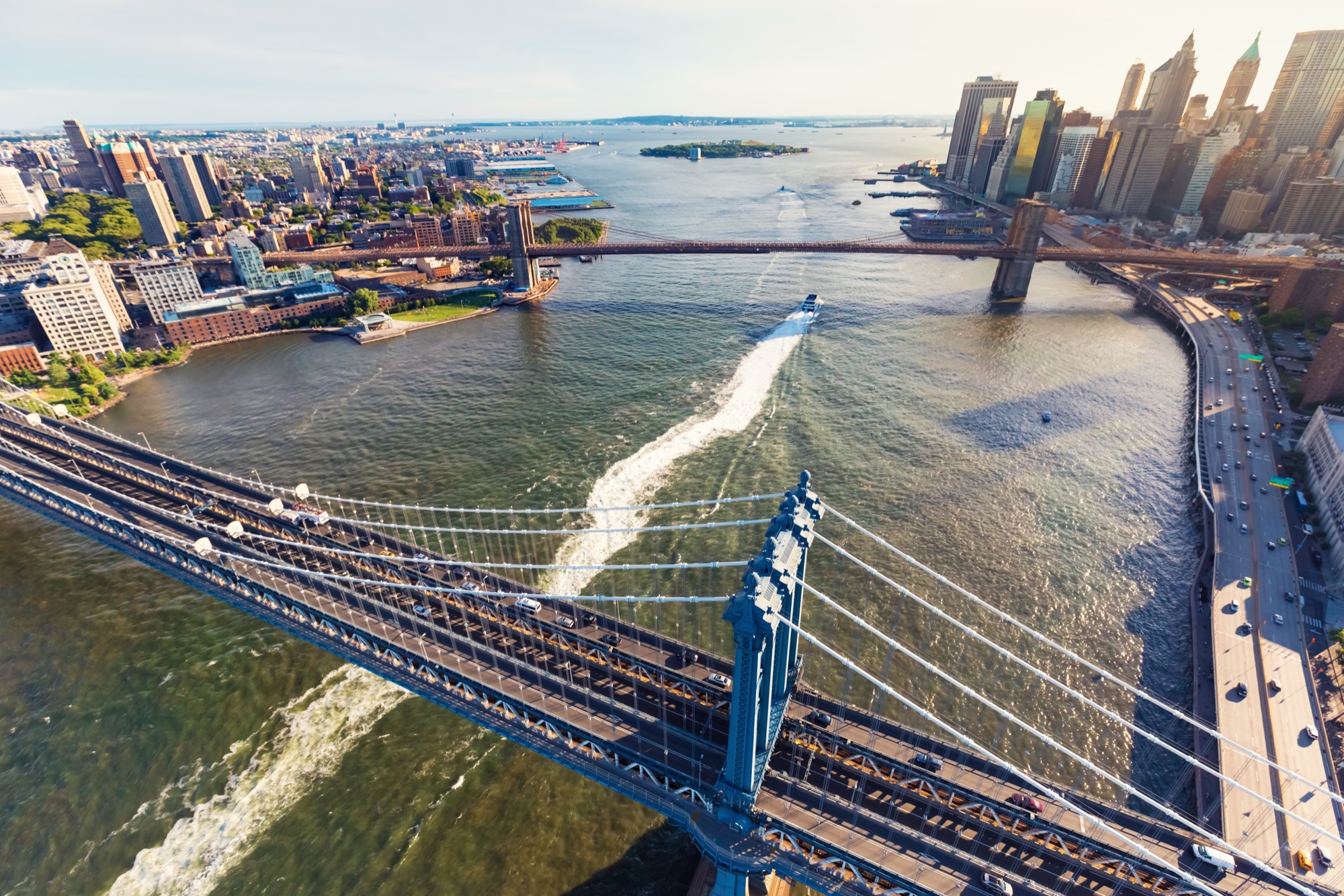 An aerial view of the Manhattan Bridge crossing the East River at sunset, with the city behind it.