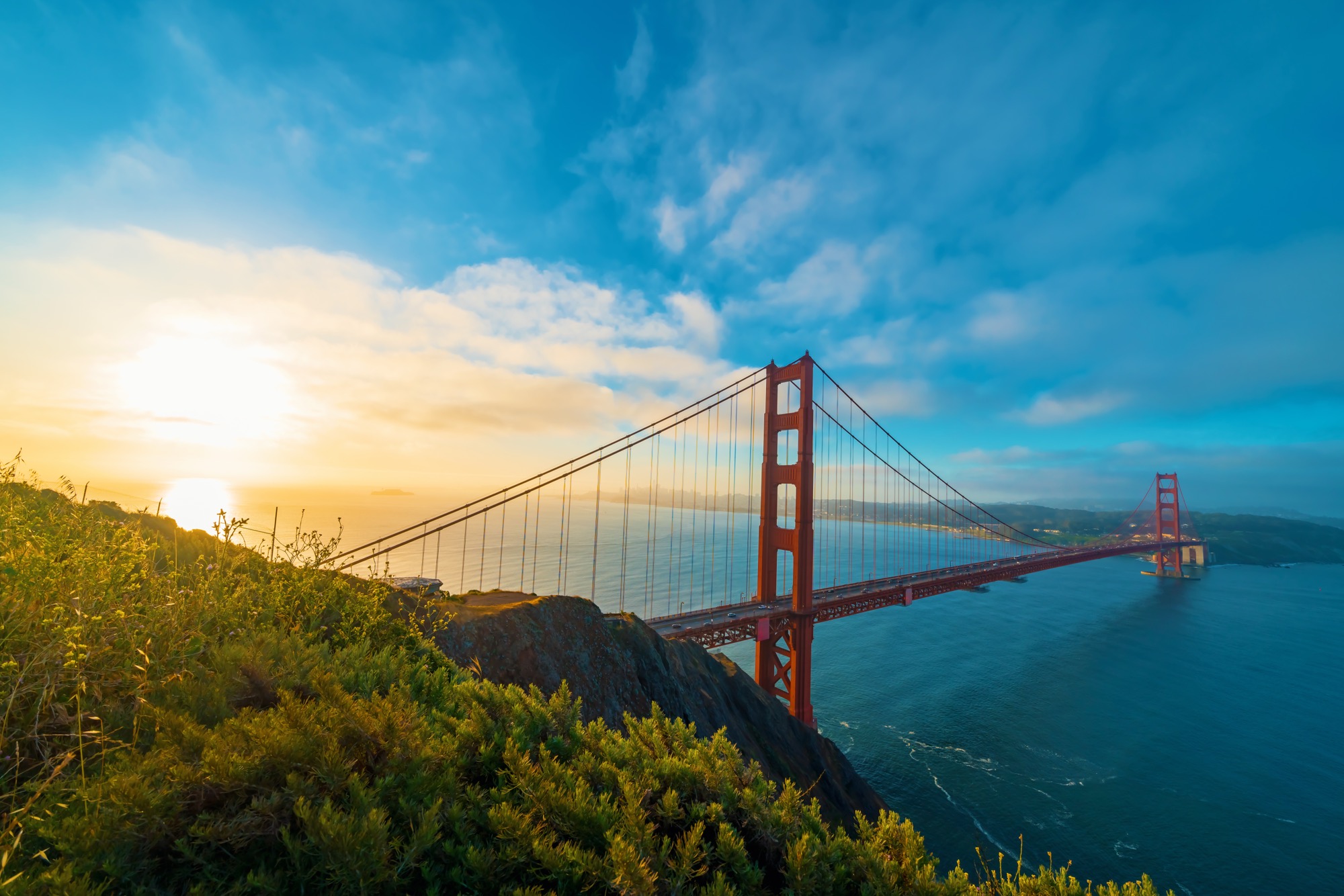 The Golden Gate Bridge at sunrise with the bay below and San Francisco in the distance.