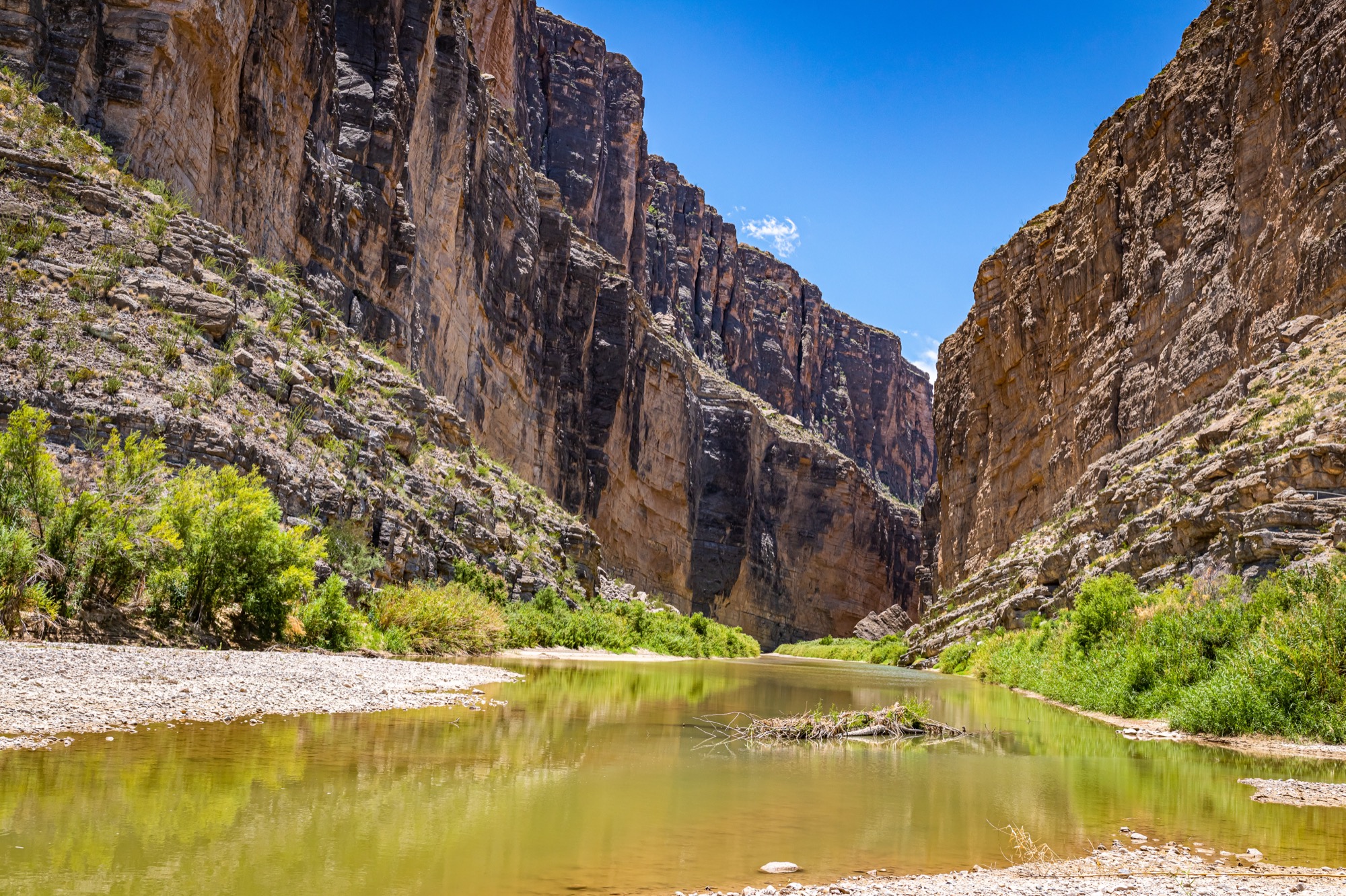 A river running between sheer limestone canyon walls under a blue sky.
