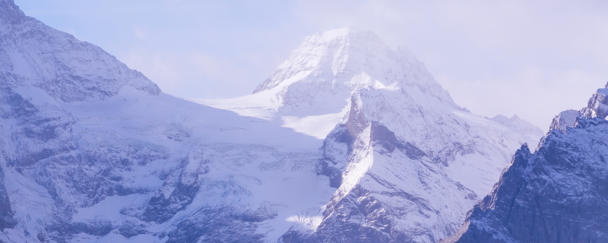 A wide view of snow-covered Alpine peaks at sunrise.
