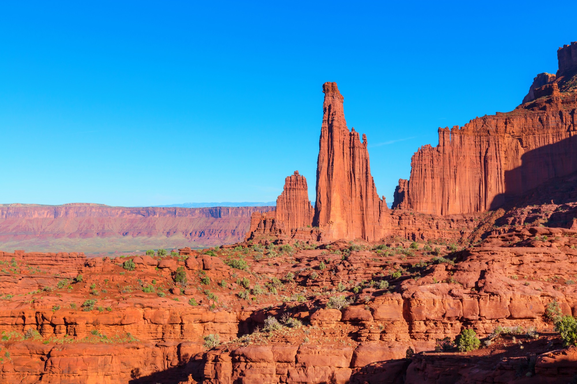 Tall red sandstone towers rising above a desert valley in Utah under a clear sky.